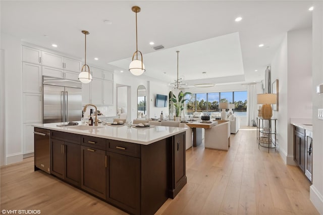 kitchen featuring stainless steel built in refrigerator, sink, decorative light fixtures, white cabinets, and light hardwood / wood-style floors