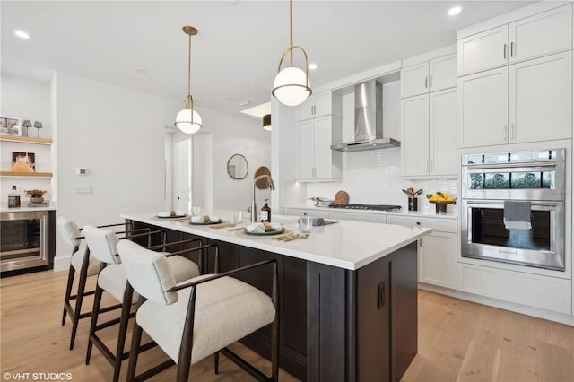 kitchen featuring pendant lighting, white cabinetry, wall chimney range hood, and appliances with stainless steel finishes