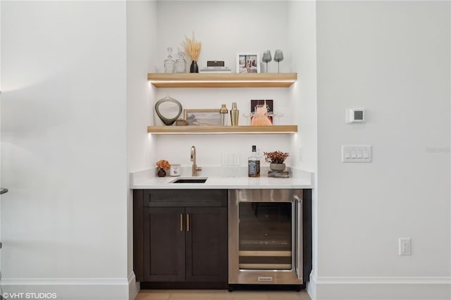 bar with dark brown cabinets, light tile patterned floors, beverage cooler, and sink