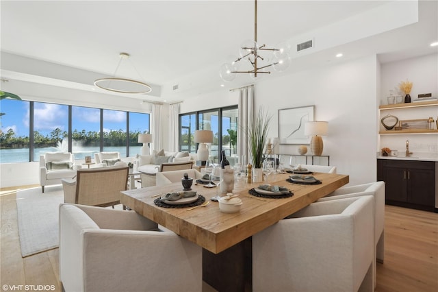 dining room with light wood-type flooring, a water view, a notable chandelier, and sink