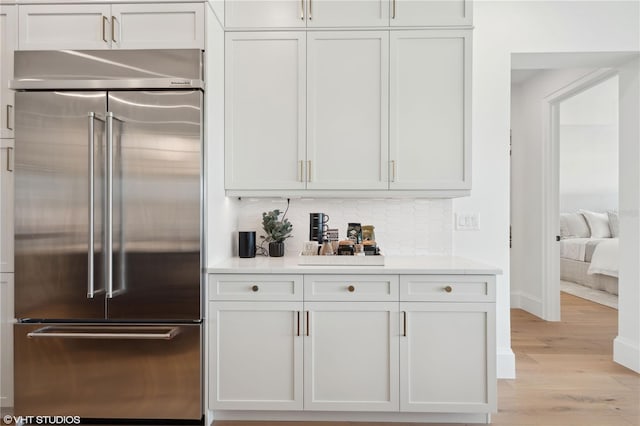 bar with high end refrigerator, light hardwood / wood-style flooring, and white cabinets