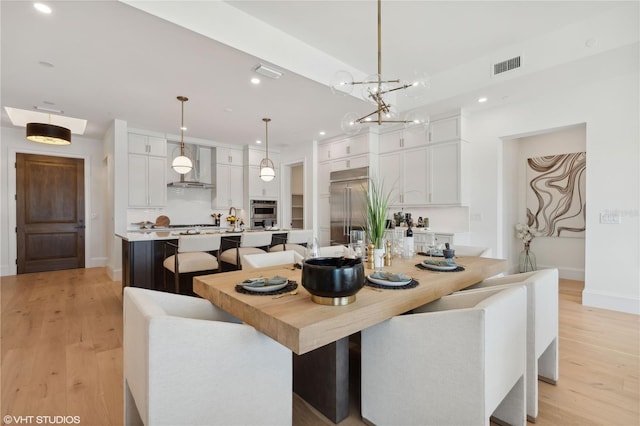 kitchen with wall chimney range hood, light wood-type flooring, appliances with stainless steel finishes, decorative light fixtures, and white cabinetry