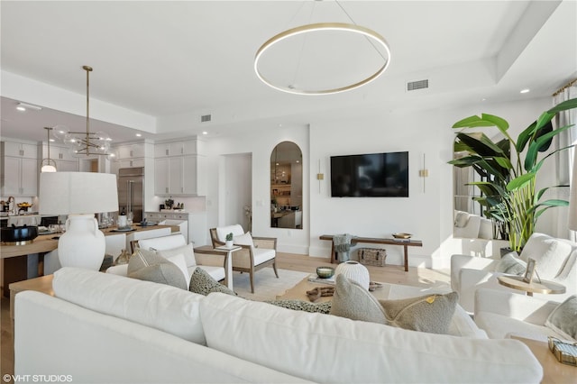 living room with a raised ceiling, light hardwood / wood-style flooring, and an inviting chandelier