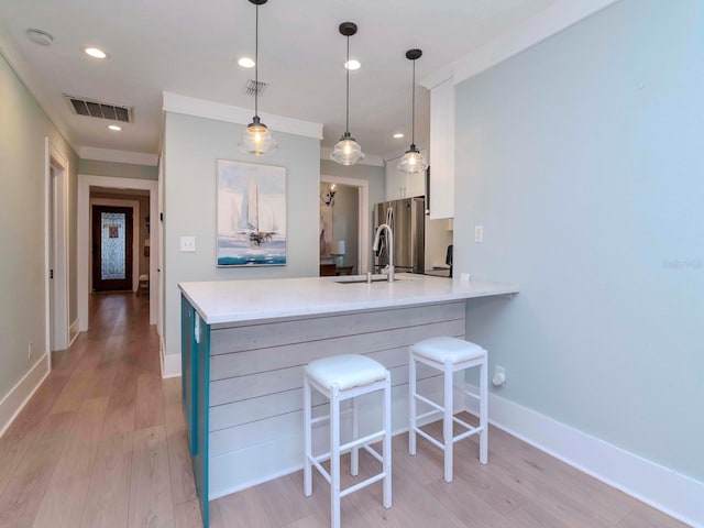 kitchen with a breakfast bar, decorative light fixtures, kitchen peninsula, light hardwood / wood-style floors, and white cabinets