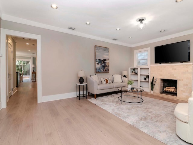 living room featuring a tiled fireplace, crown molding, a healthy amount of sunlight, and light wood-type flooring