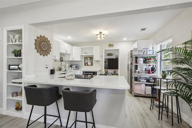 kitchen featuring white cabinets, light hardwood / wood-style flooring, black electric cooktop, a kitchen bar, and kitchen peninsula