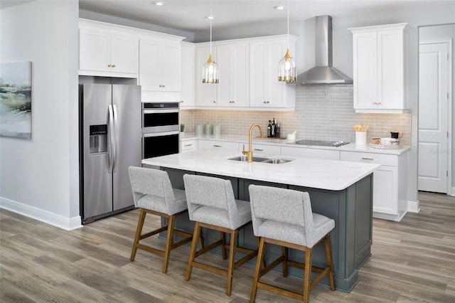 kitchen featuring a center island with sink, wall chimney exhaust hood, sink, and appliances with stainless steel finishes