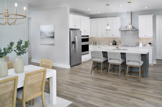 kitchen with wall chimney exhaust hood, light hardwood / wood-style flooring, pendant lighting, white cabinets, and appliances with stainless steel finishes