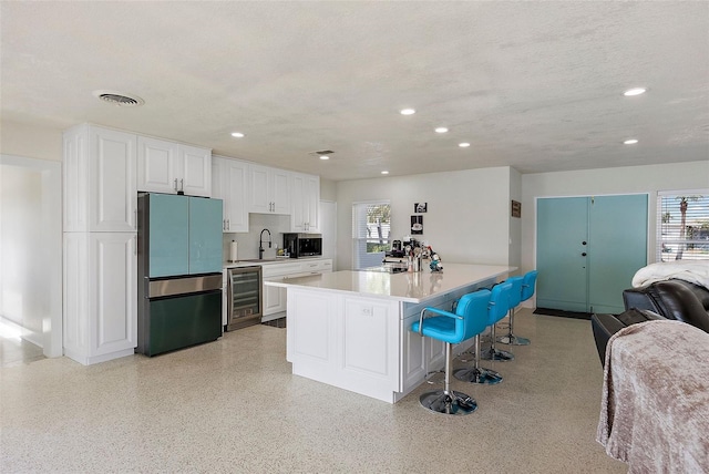 kitchen featuring a breakfast bar, white cabinetry, refrigerator, and wine cooler