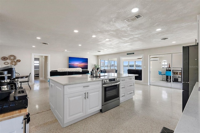 kitchen with stainless steel range with electric stovetop, white cabinetry, a wall unit AC, a textured ceiling, and a center island