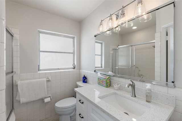 bathroom featuring a shower with shower door, vanity, tile walls, and toilet