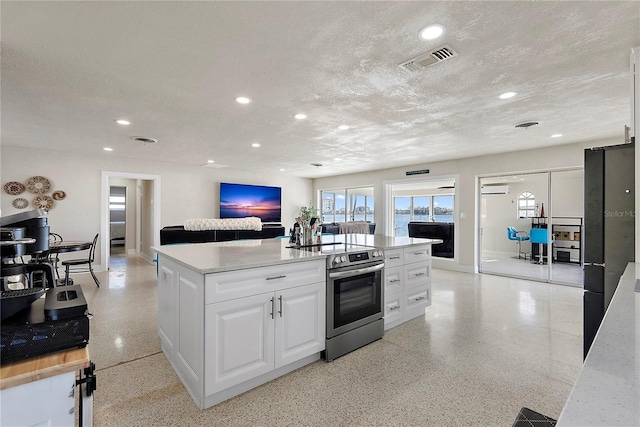 kitchen featuring an AC wall unit, a kitchen island, stainless steel electric range, a textured ceiling, and white cabinets