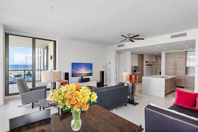 living room featuring light tile patterned floors, a wall of windows, ceiling fan, and sink