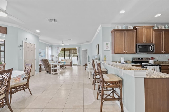 kitchen with light stone countertops, appliances with stainless steel finishes, ceiling fan, and ornamental molding