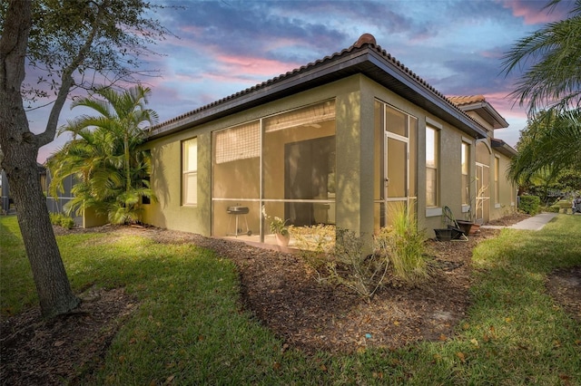 property exterior at dusk featuring a lawn and a sunroom