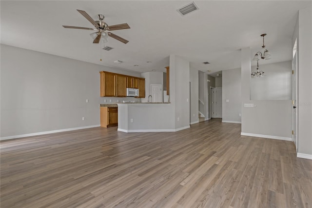 unfurnished living room featuring ceiling fan with notable chandelier and light hardwood / wood-style floors