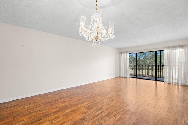 spare room with light hardwood / wood-style flooring, a textured ceiling, and a notable chandelier