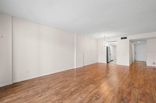 unfurnished room with a chandelier, wood-type flooring, and a textured ceiling