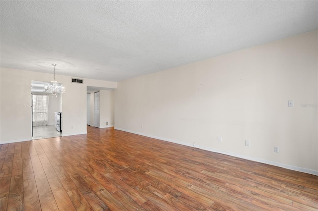 spare room with a chandelier, a textured ceiling, and light hardwood / wood-style floors