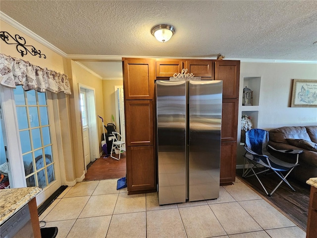 kitchen featuring light stone counters, light tile patterned floors, ornamental molding, and stainless steel refrigerator