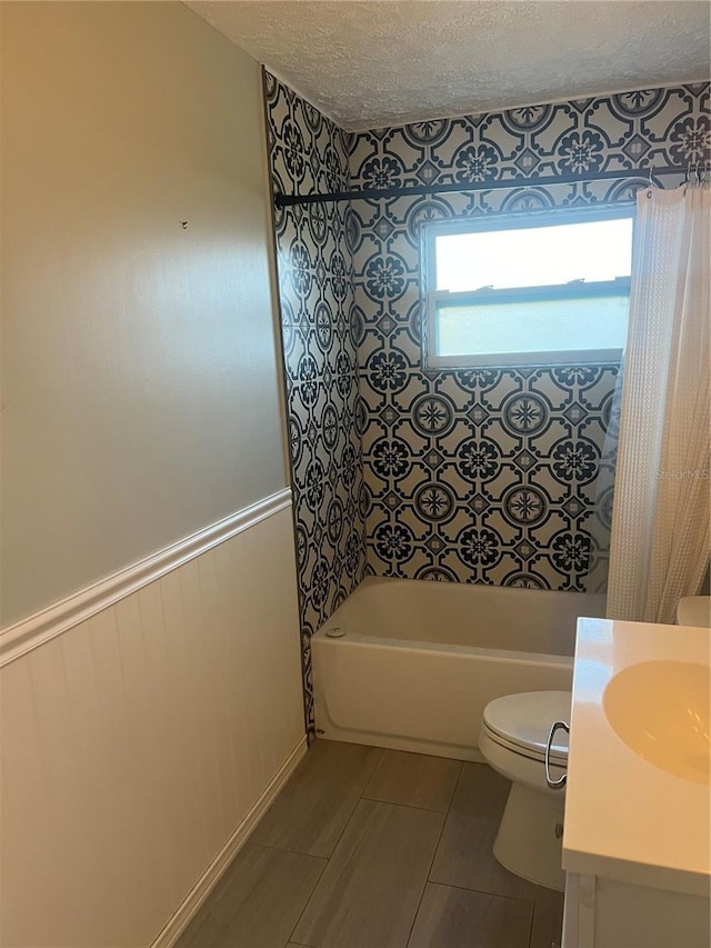 full bathroom featuring a textured ceiling, vanity, toilet, and tiled shower / bath combo