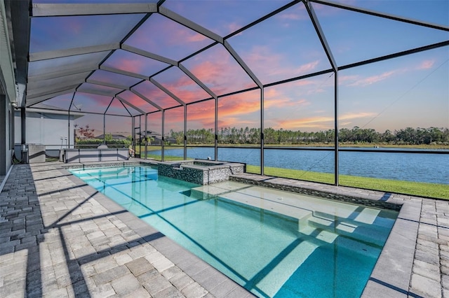 pool at dusk with glass enclosure, an in ground hot tub, a patio area, and a water view