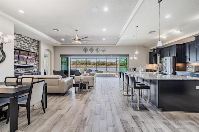 kitchen with ceiling fan, light stone counters, light hardwood / wood-style flooring, decorative light fixtures, and a kitchen bar