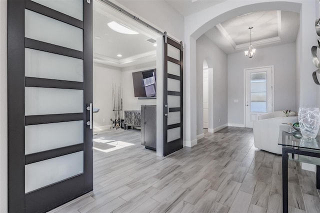 foyer entrance with a tray ceiling, a barn door, light hardwood / wood-style floors, and a notable chandelier