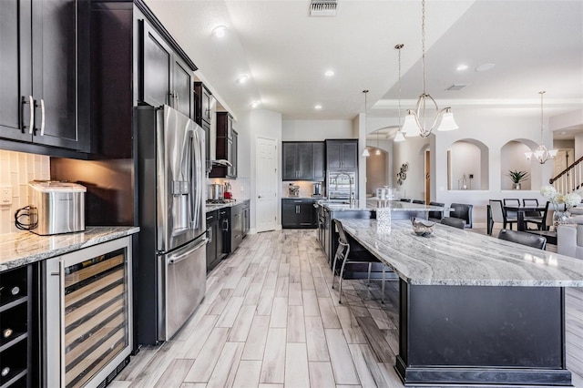 kitchen featuring wine cooler, decorative light fixtures, stainless steel fridge with ice dispenser, and a large island with sink