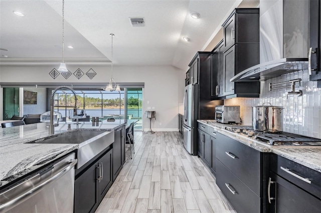 kitchen with light stone countertops, tasteful backsplash, wall chimney exhaust hood, stainless steel appliances, and decorative light fixtures