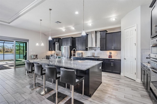 kitchen with a large island with sink, a breakfast bar, wall chimney exhaust hood, and hanging light fixtures