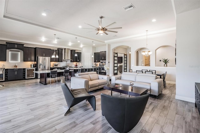 living room featuring ceiling fan with notable chandelier, light wood-type flooring, beverage cooler, and crown molding