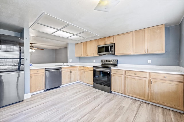 kitchen featuring a sink, light countertops, appliances with stainless steel finishes, light wood-type flooring, and light brown cabinetry