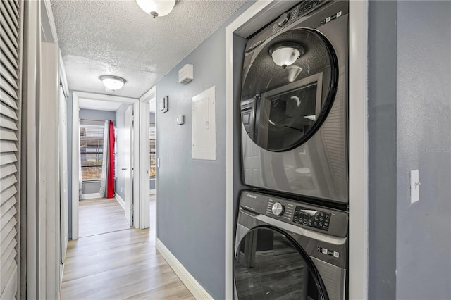 clothes washing area with a textured ceiling, light hardwood / wood-style flooring, and stacked washer / dryer