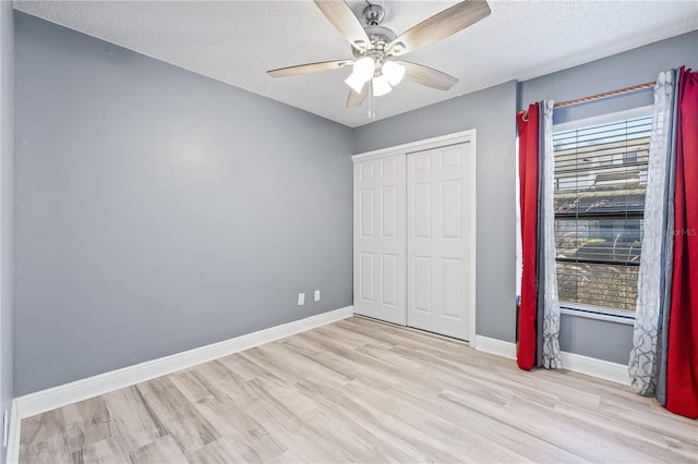 unfurnished bedroom with a closet, ceiling fan, a textured ceiling, wood finished floors, and baseboards