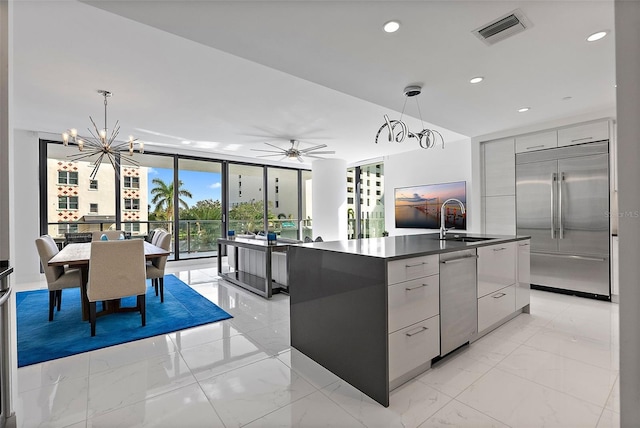 kitchen featuring sink, pendant lighting, a kitchen island with sink, ceiling fan with notable chandelier, and appliances with stainless steel finishes