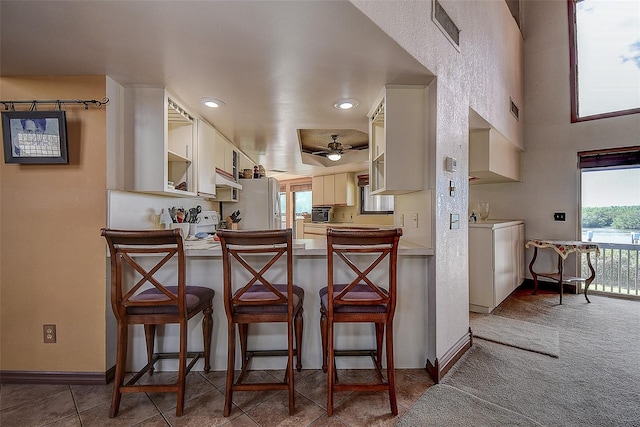 kitchen with washer / dryer, dark tile patterned flooring, a wealth of natural light, and a kitchen breakfast bar