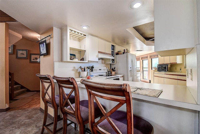 kitchen with kitchen peninsula, a kitchen breakfast bar, white appliances, dark tile patterned floors, and white cabinets