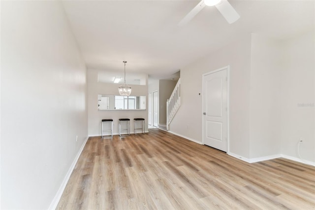 unfurnished living room with ceiling fan with notable chandelier and light hardwood / wood-style floors