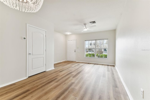 unfurnished room with ceiling fan with notable chandelier and light hardwood / wood-style flooring