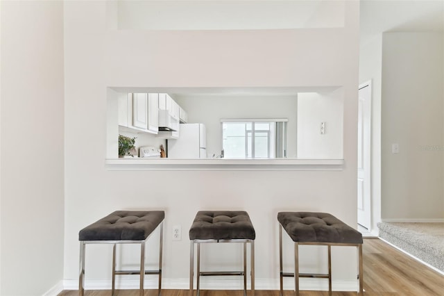 interior space with white cabinetry, white fridge, extractor fan, and a kitchen breakfast bar