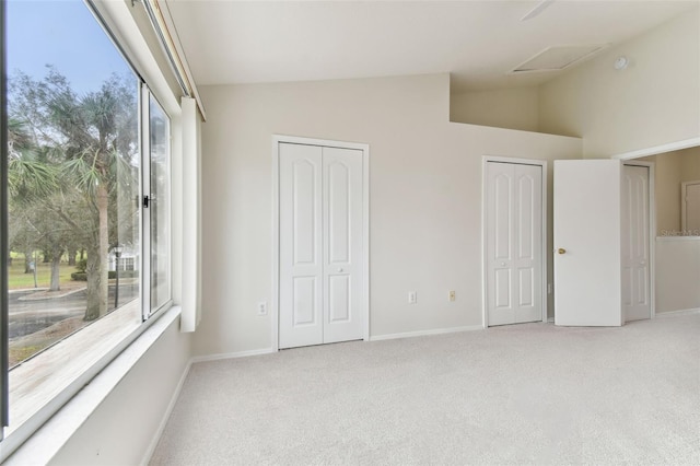 unfurnished bedroom featuring light colored carpet, vaulted ceiling, and two closets