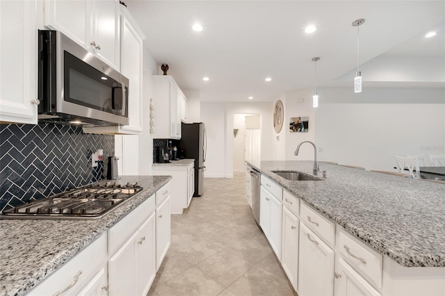 kitchen with light stone countertops, pendant lighting, stainless steel appliances, white cabinetry, and sink