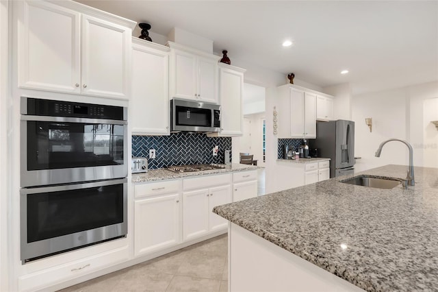 kitchen with stainless steel appliances, white cabinetry, sink, and light stone countertops