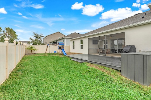 view of yard featuring a wooden deck, a playground, and a sunroom