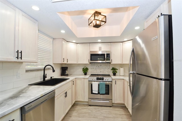 kitchen featuring sink, stainless steel appliances, light hardwood / wood-style flooring, backsplash, and a tray ceiling