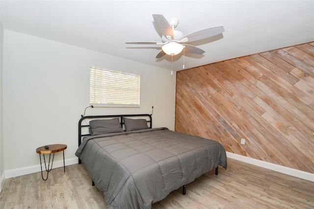 bedroom with ceiling fan, light hardwood / wood-style flooring, and wood walls