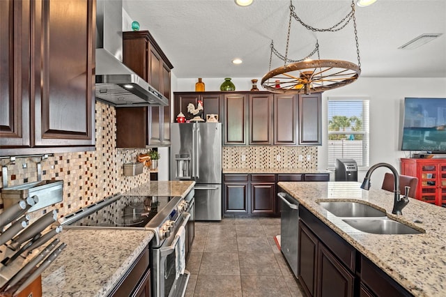 kitchen with light stone countertops, sink, stainless steel appliances, wall chimney range hood, and a textured ceiling