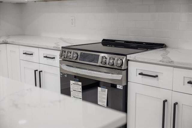 kitchen featuring stainless steel electric stove, decorative backsplash, white cabinetry, and light stone counters