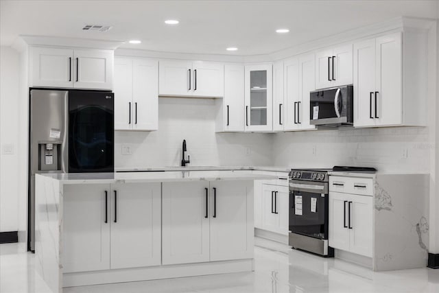 kitchen featuring a kitchen island, appliances with stainless steel finishes, backsplash, and white cabinetry